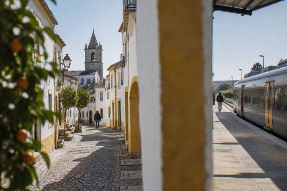 A railway platform in Évora with a regional train waiting under a clear afternoon sky