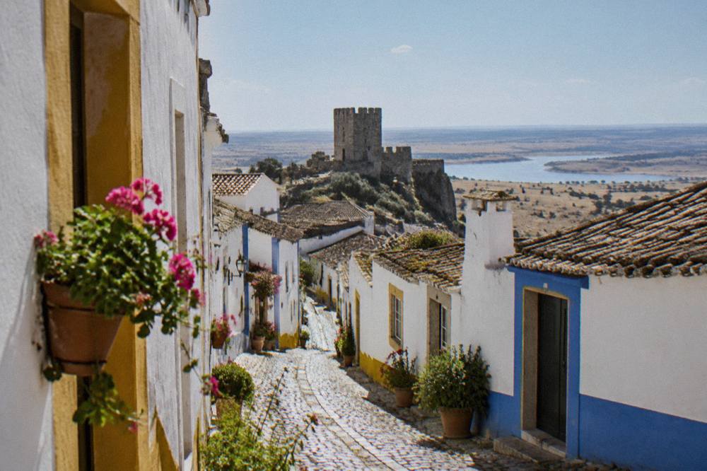 Narrow whitewashed street in an Alentejo hill town with blue and yellow trim and potted flowers