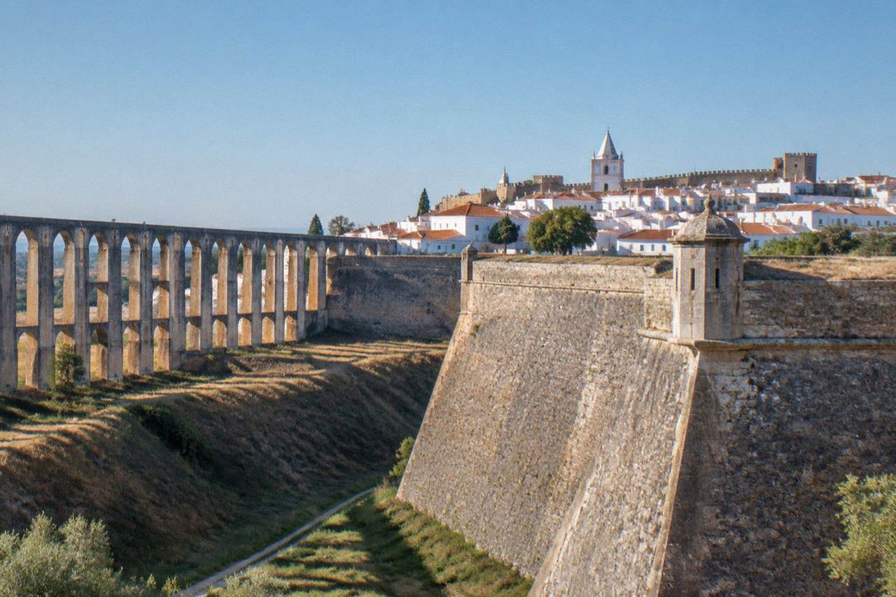 A walled Alentejo hill town with a church tower and crenellated ramparts under a blue sky