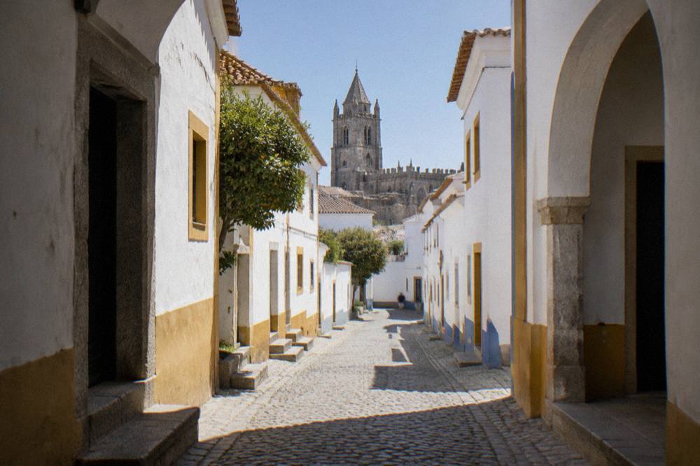 A narrow whitewashed street inside the walls of Évora with the cathedral tower in the background