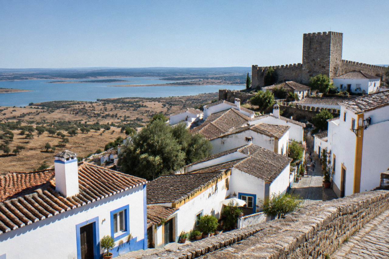 A walled hilltop village with whitewashed houses overlooking a wide plain and a large lake