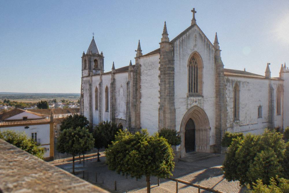 Sunlight falling on the worn stone facade of a Gothic church in a small Portuguese city square