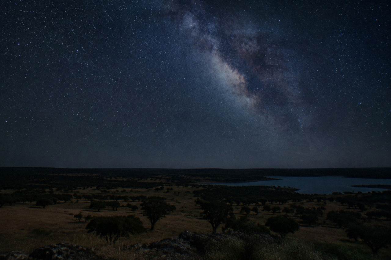 A wide night sky full of stars above the dark silhouette of Alentejo countryside