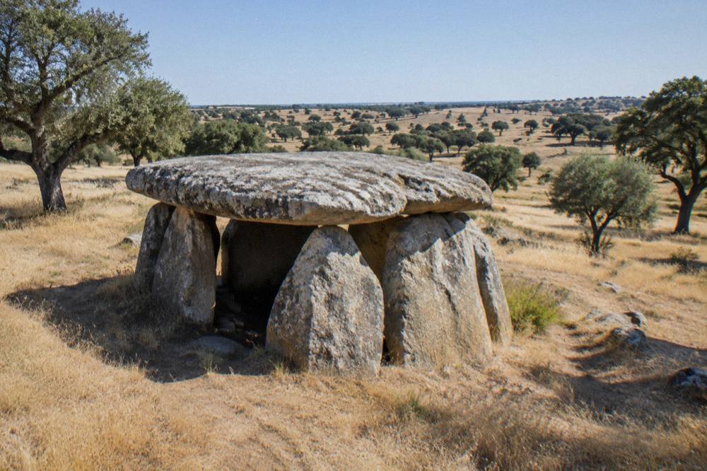 A large stone dolmen chamber standing in dry golden grassland under a wide sky in the Alentejo
