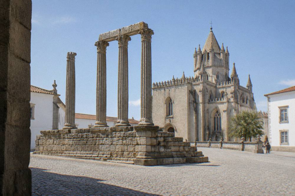 The granite columns of the Roman temple in Évora rising above a cobbled square with the cathedral behind