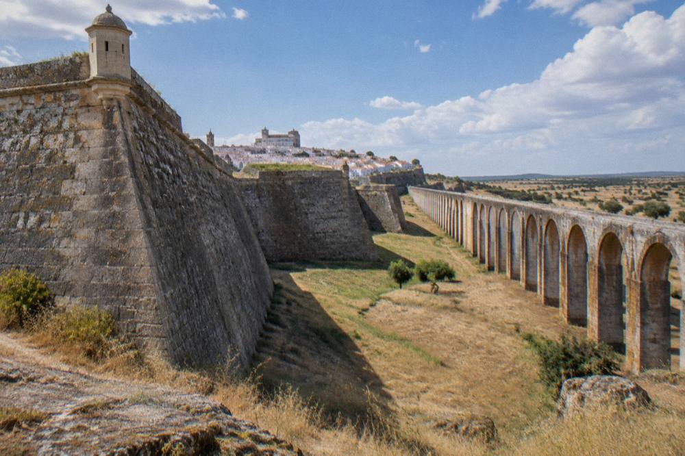 A long stone aqueduct of many arches crossing dry open countryside toward a distant walled town