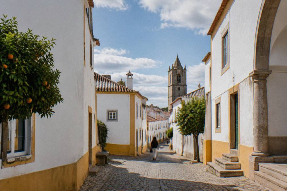 White-washed houses and a church tower seen from a narrow street inside the walls of Évora