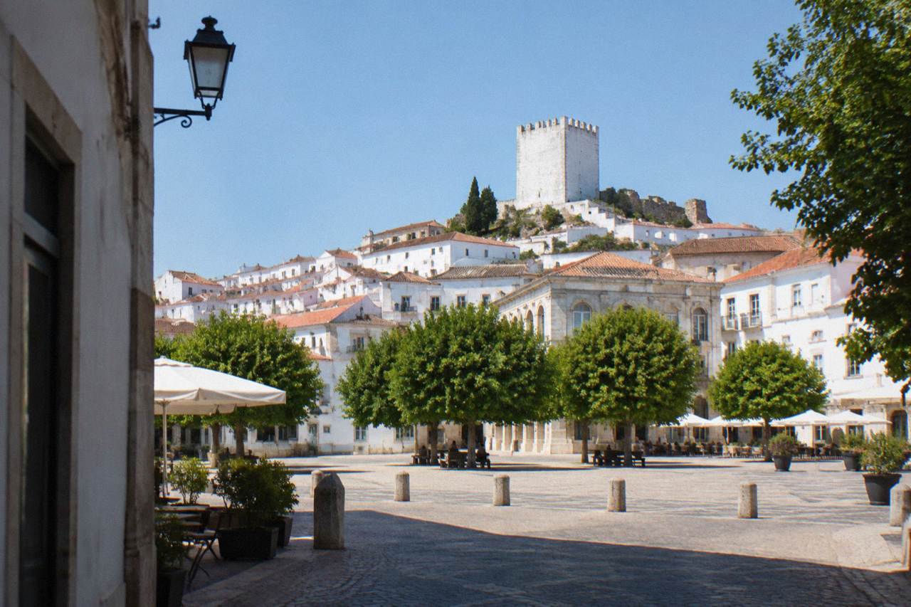 A hilltop Alentejo town with white marble buildings and a castle tower rising above the surrounding plain