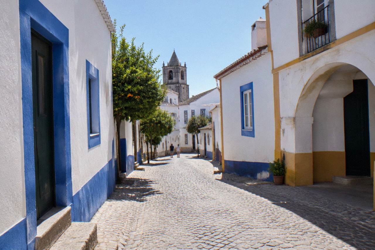 A quiet cobbled street inside the walled historic centre of Évora with whitewashed houses and blue-trimmed doorways