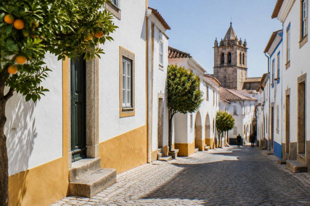 Sunlight falling across whitewashed houses and a church tower inside the walls of Évora