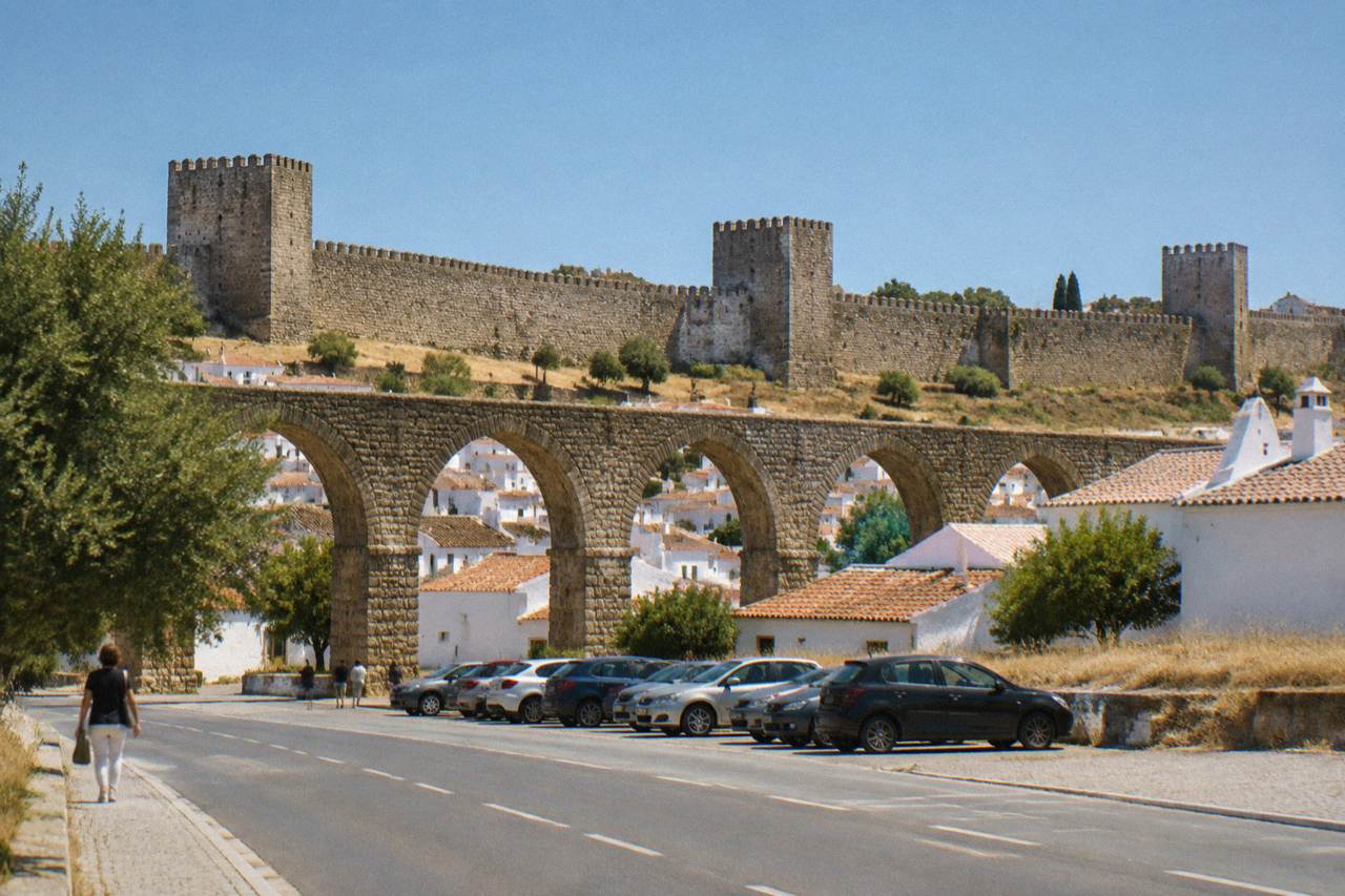 The stone arches of an old aqueduct passing between low white houses on the edge of a Portuguese town