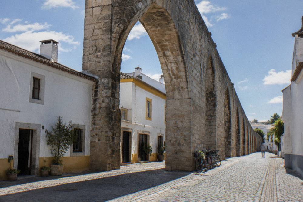 A tall stone arch of the aqueduct spanning a narrow street with parked bicycles