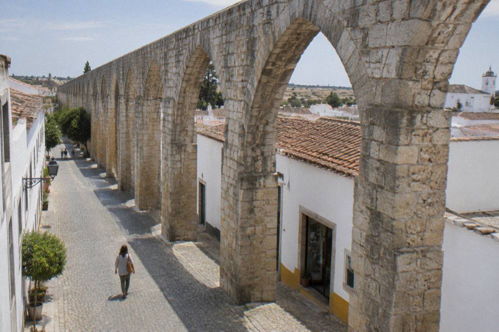 A visitor walking a cobbled street with an arch of the aqueduct overhead