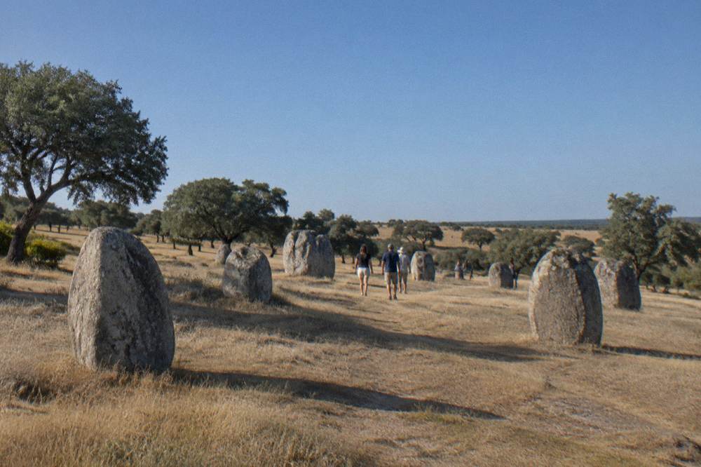 A small group of visitors walking among the standing stones on the open Alentejo hillside