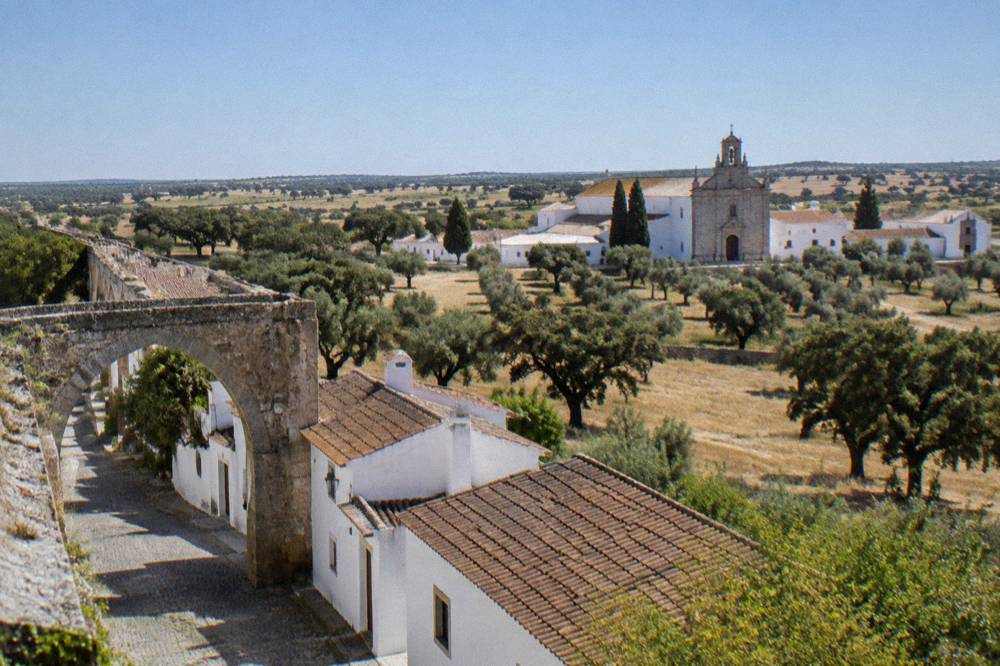 A stone aqueduct arch with houses built against it, on the walking route toward the Cartuxa estate