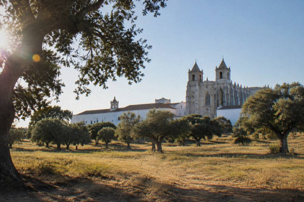 A large stone cathedral with twin towers and buttresses seen from a narrow street in Évora
