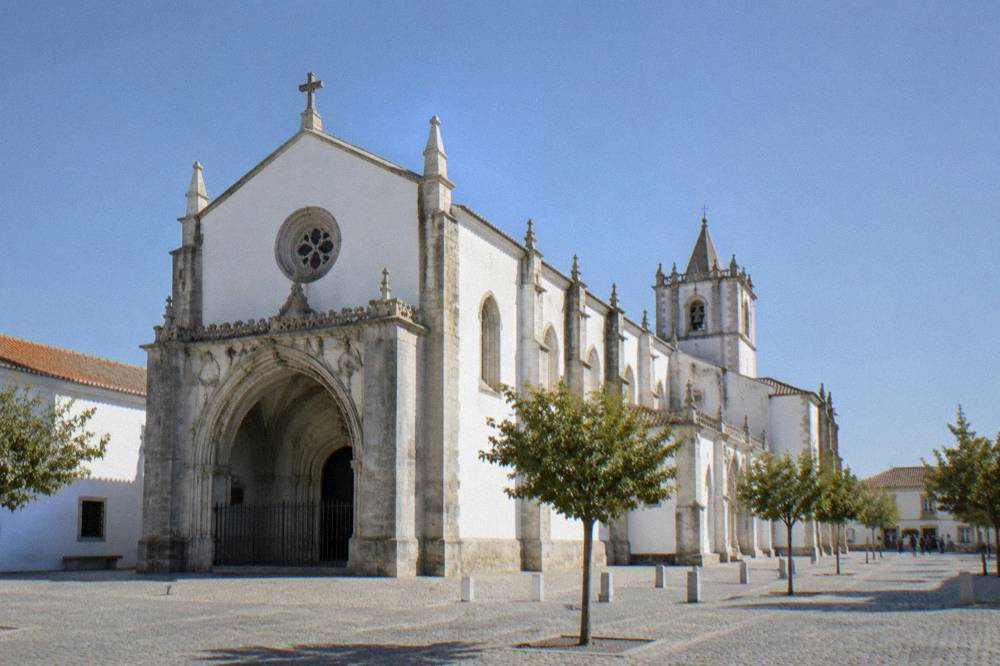 The exterior of the Igreja de São Francisco in Évora with its Gothic and Manueline arcade and a few visitors far off
