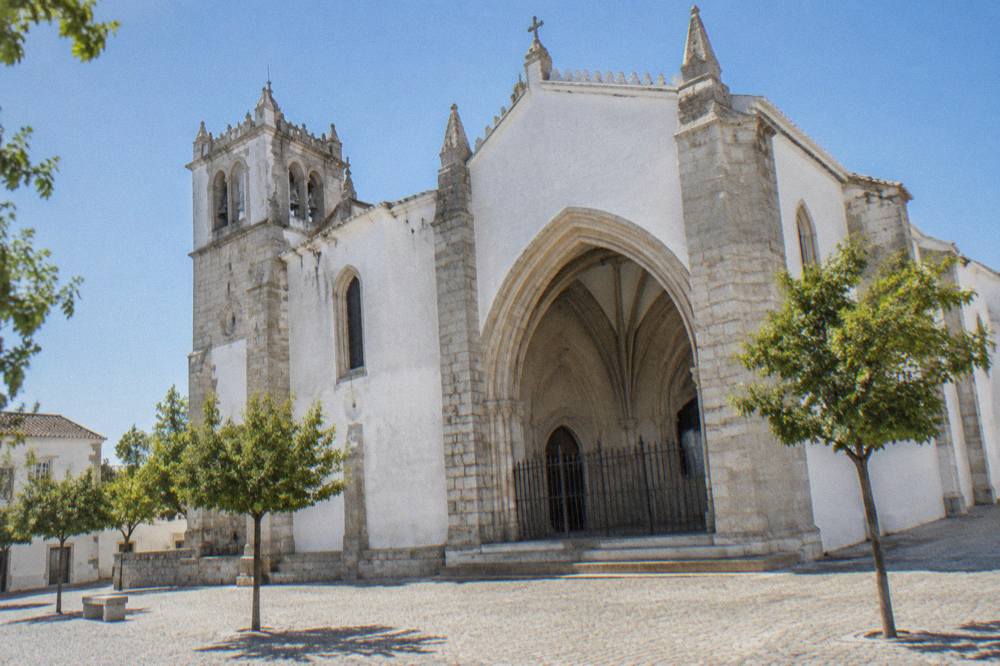 The pale stone facade of the Igreja de São Francisco in Évora under a clear sky, seen from the square outside