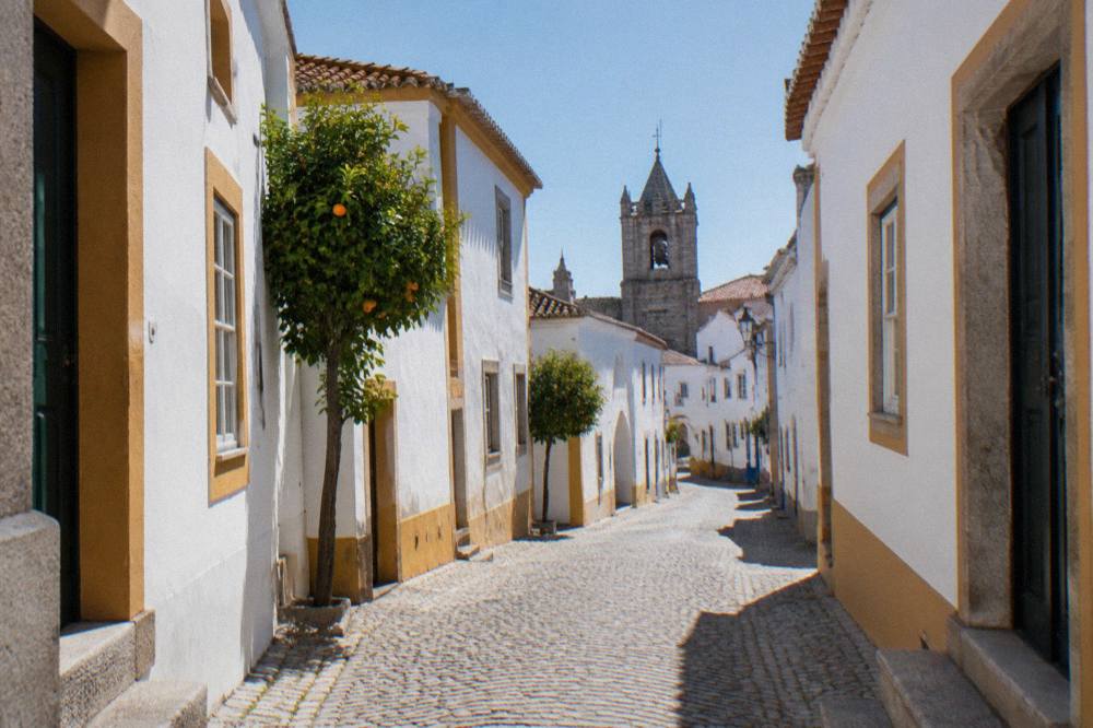 A narrow cobbled street in Évora leading toward an old palace tower with white walls