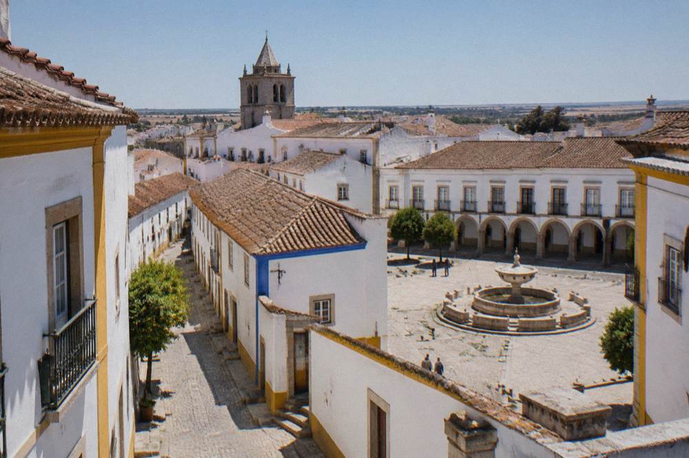 A stone fountain and arcaded buildings in the main square of Évora under a clear sky