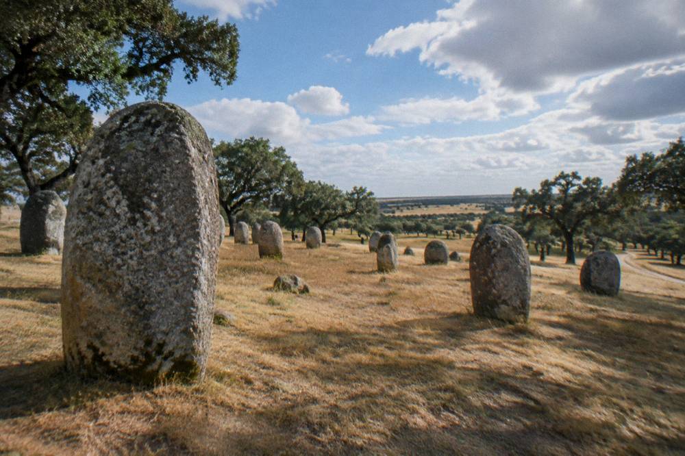 Standing stones of the Almendres cromlech on a grassy slope under a wide sky