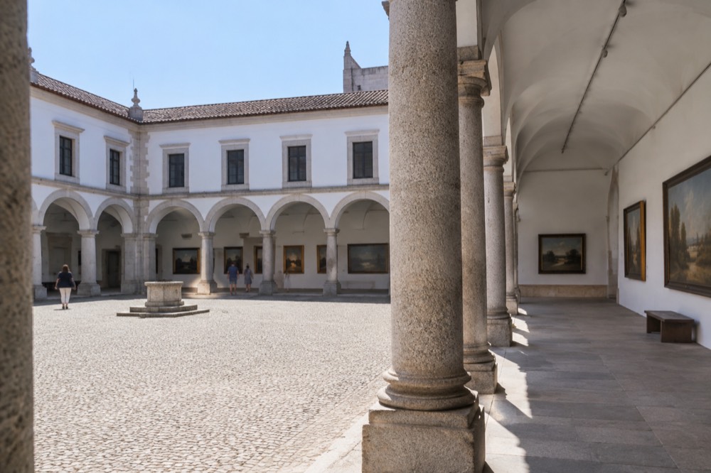 Sunlit museum gallery with stone columns and paintings on pale walls