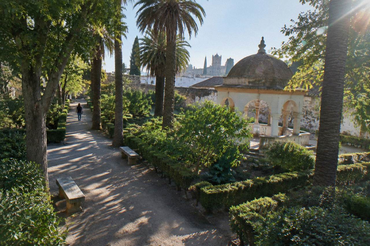 Shaded gravel path in a public garden in Évora with stone benches and old walls in the background