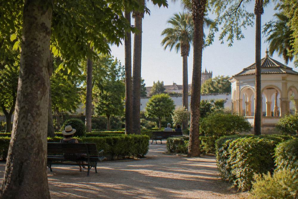People resting on benches under shade in a public garden in Évora