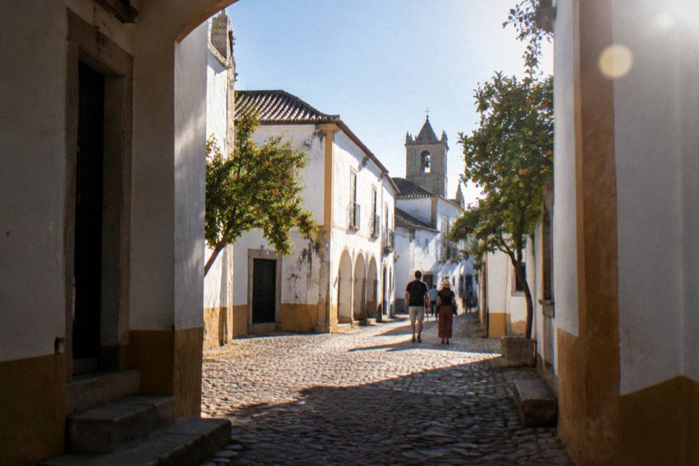 Travellers walking a sunlit cobbled lane between whitewashed buildings in Évora's old town