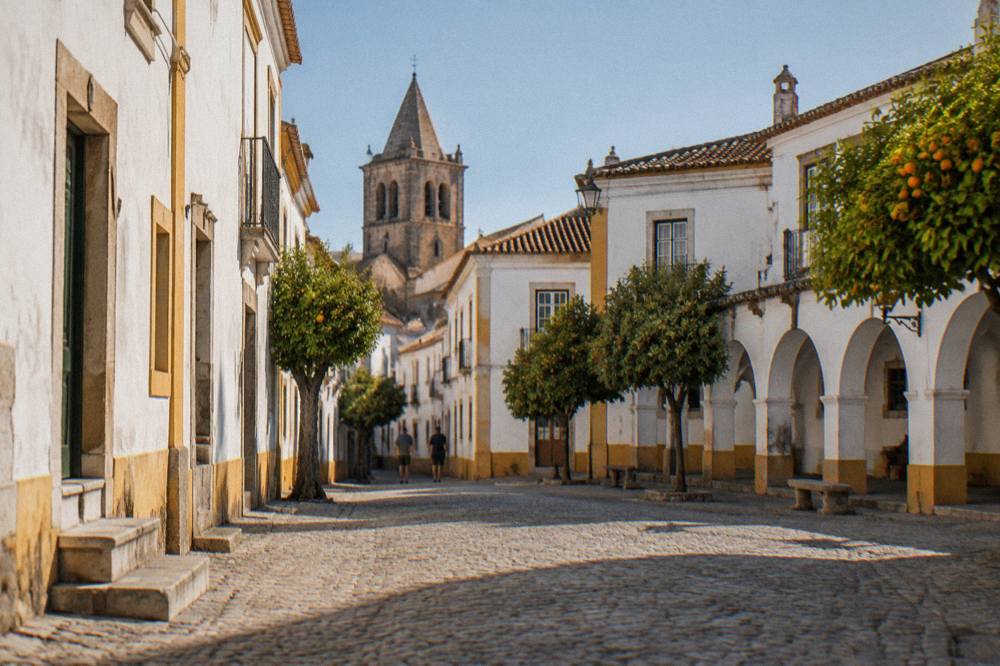 A quiet square in Évora with white arcades and a church tower in afternoon light