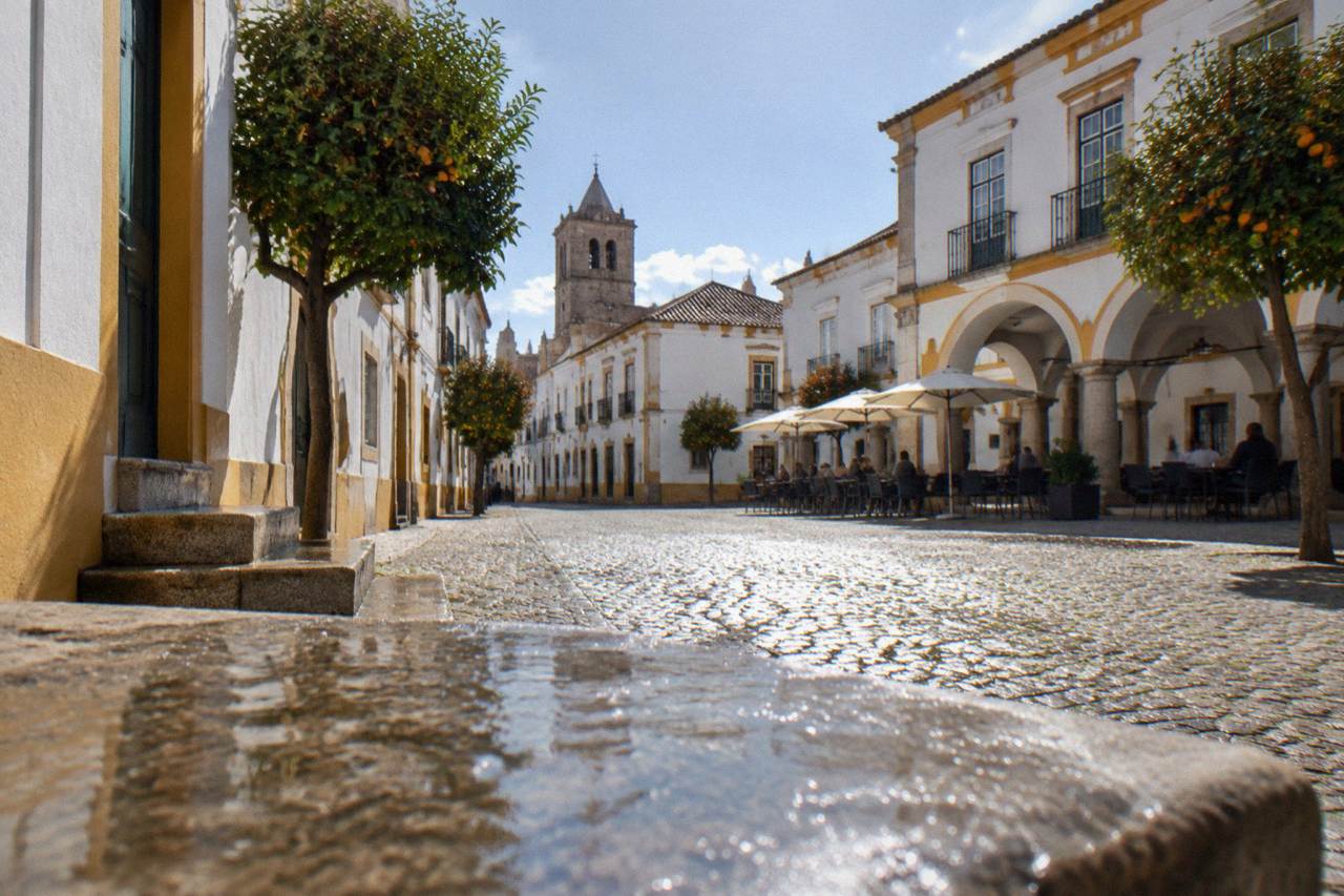 A wide open public square in Évora with arcaded buildings on one side and outdoor tables in the shade