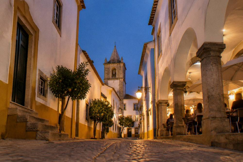 People seated at outdoor cafe tables under the arcades of a Portuguese town square at dusk