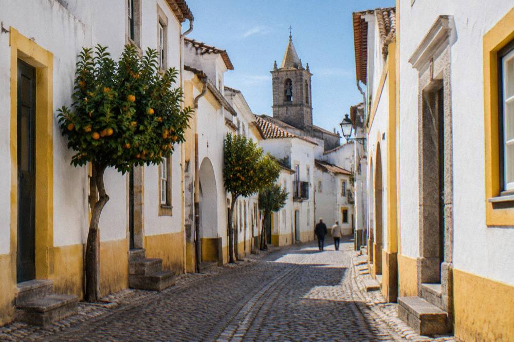 Cobbled street in Évora with white walls, yellow trim and a distant bell tower