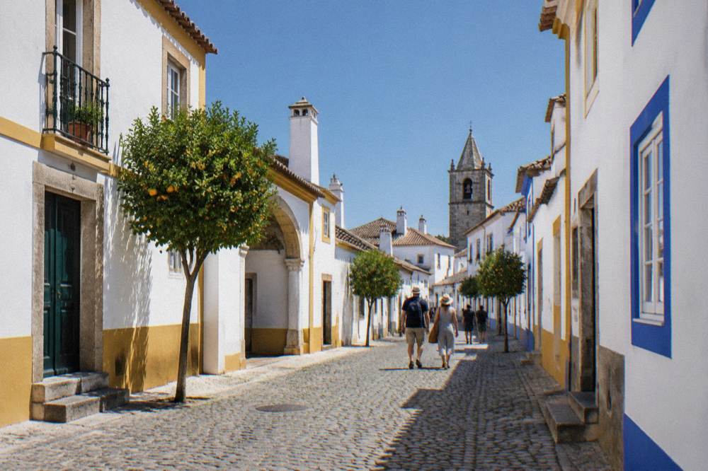 Visitors walking a narrow cobbled street in Évora beneath church towers and chimneys