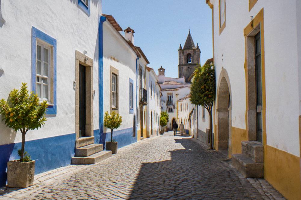 Sunlit cobbled street with white walls and blue trim in central Évora
