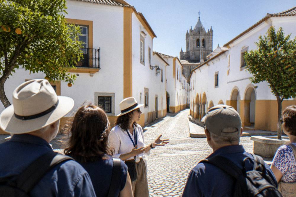 A guide speaking to a small group of visitors on a cobbled square in Évora