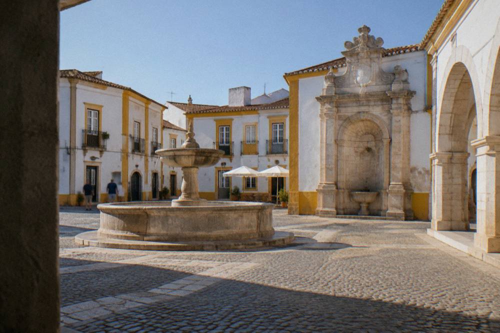 A carved limestone Renaissance fountain with a niche and heraldic detail in a small Alentejo square