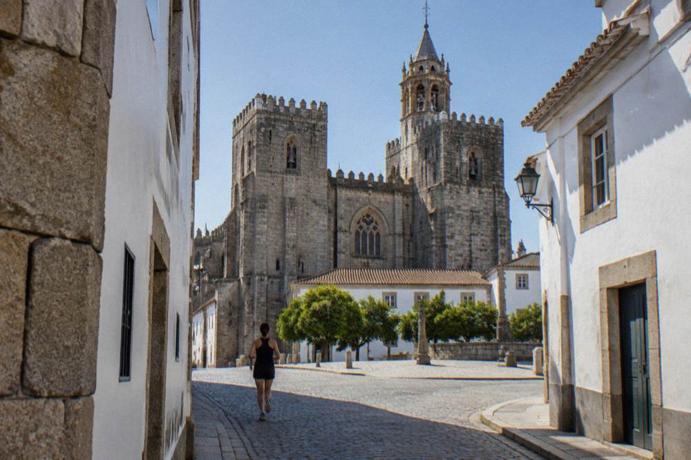 The Gothic cathedral of Évora seen from a narrow street with granite and whitewashed walls in warm afternoon light