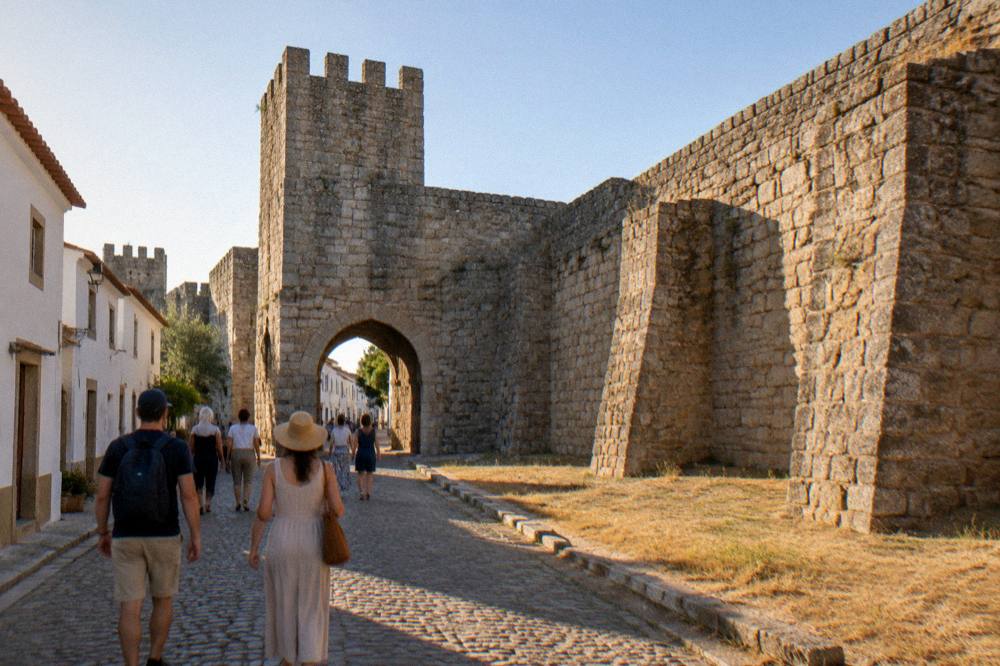 Visitors walking a cobbled street in Évora past the granite arches and buttresses of the old city walls