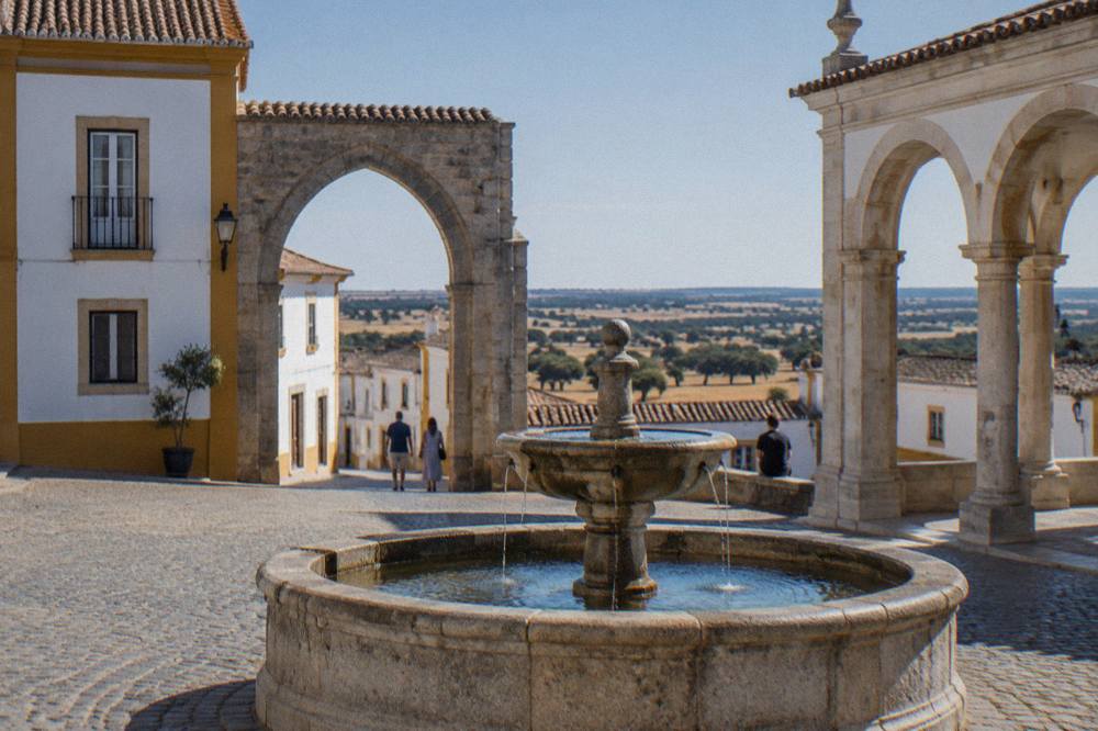 A wide Alentejo landscape of cork oaks and wheat fields under a clear sky beyond the rooftops of Évora