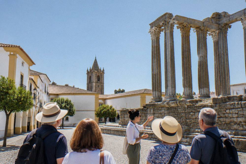 A guide speaking to a small group beside the temple columns in Évora