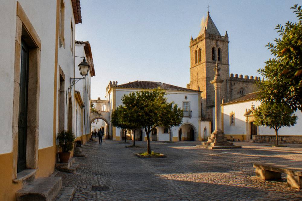 Golden evening light across an open square in Évora with a stone chapel tower rising against the sky