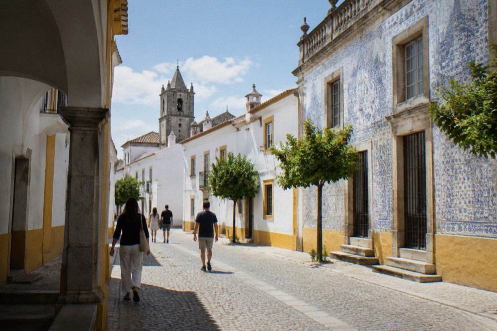 Visitors walking past the tiled university facade on a bright morning in Évora