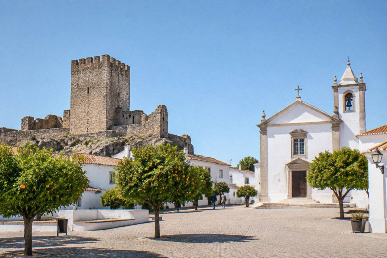 A small Alentejo hill town with a stone castle tower above low white houses under a wide blue sky