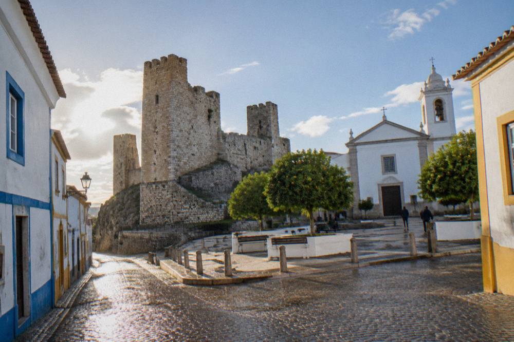 Whitewashed houses with blue and yellow trim along a narrow Alentejo street in strong afternoon light