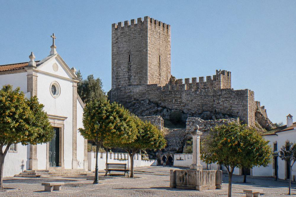 A stone castle keep with battlements seen from below against a clear sky in a small Portuguese town