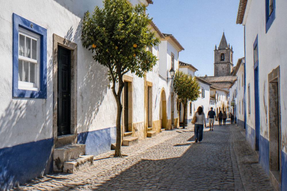Visitors walking a sunlit cobbled street in Évora's historic centre past white walls and blue trim