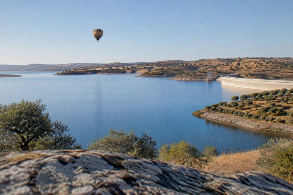 A hot air balloon drifting at dawn above the Alqueva lake and brown Alentejo hills