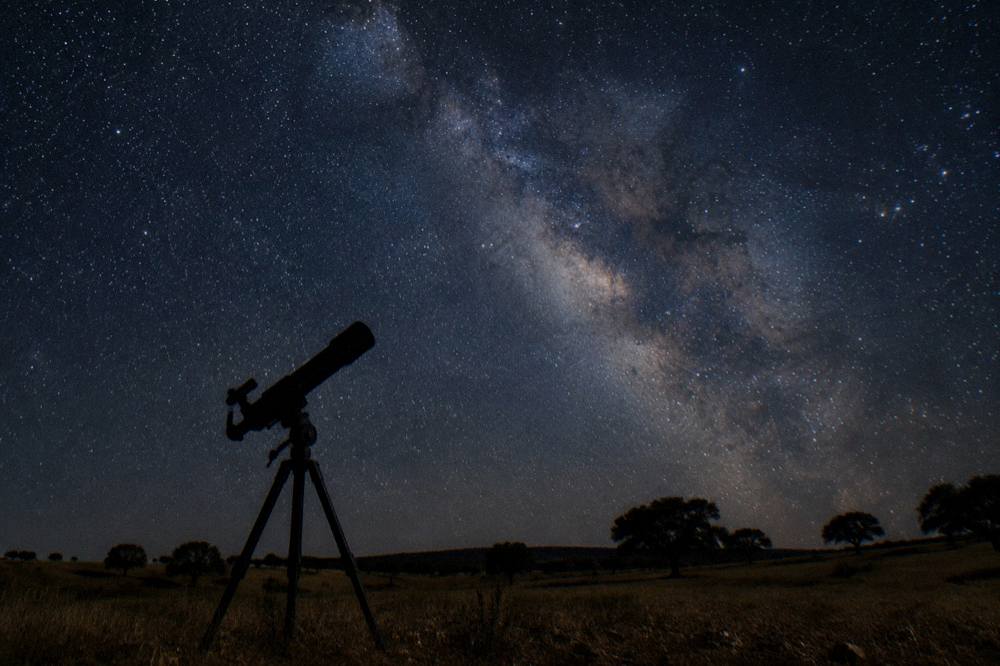 A telescope silhouette against a star filled sky over the Alentejo plain