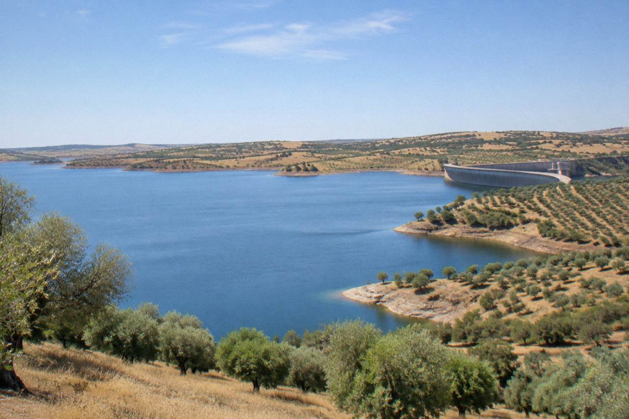Wide view over the Alqueva reservoir shoreline with calm water and rolling Alentejo hills